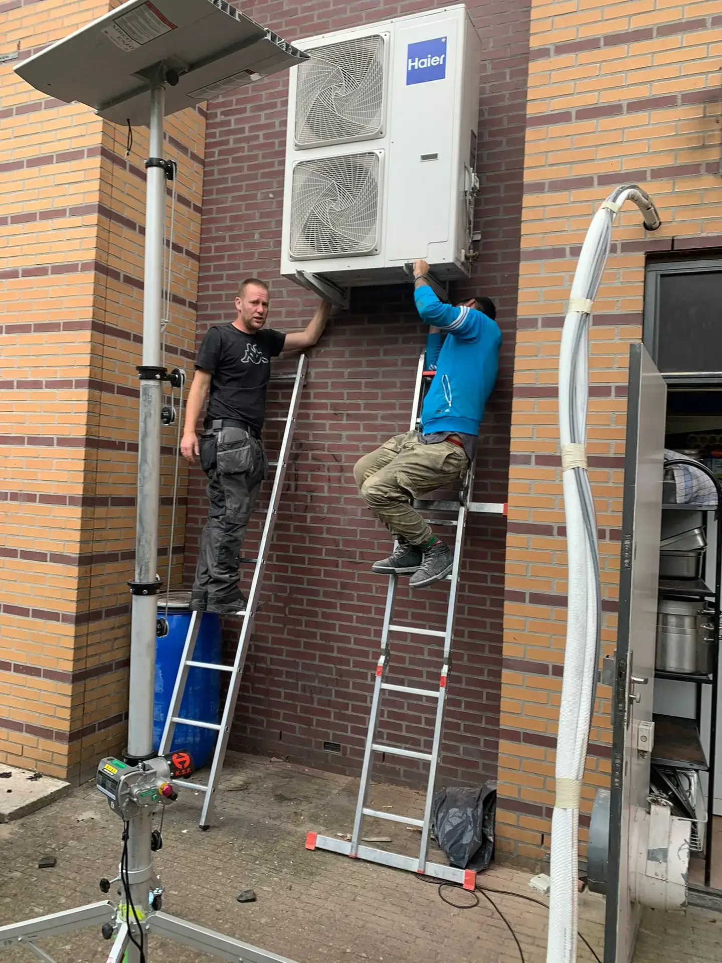 Plaatsing van zware Haier buitenunit met monteurs op ladders